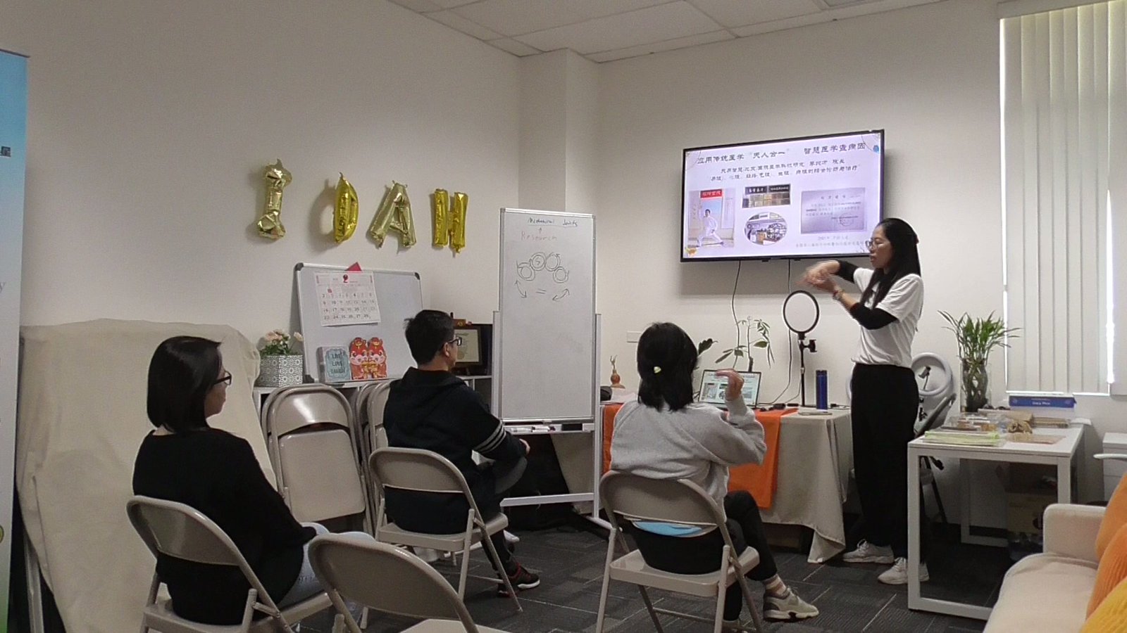 The instructor presenting to a small class at a coworking studio, students seen from behind